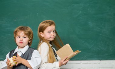 Komik küçük çocuk ve tahtayı gösteren sevimli küçük kız. Kopya alanı. Kara tahta arka planı. Okul çocukları. İlkokuldan çocuklar. İlk okul günü.