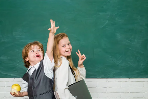Ungarna gör sig redo för skolan. Några små flickor och pojkar i klassrummet. Skolflicka hjälper elever som studerar vid skrivbord i klassrummet. Glada skolbarn. Apple och böcker - skolkoncept. — Stockfoto