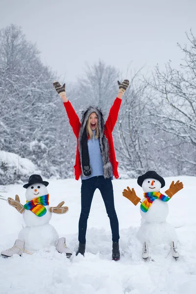 Lustiger Schneemann in stylischem Hut und Schal mit lustigen Mädchen auf schneebedecktem Feld. glückliches Mädchen, das mit einem Schneemann auf einem verschneiten Winterspaziergang posiert. glückliches Mädchen Schneemann und Winterspaß. — Stockfoto