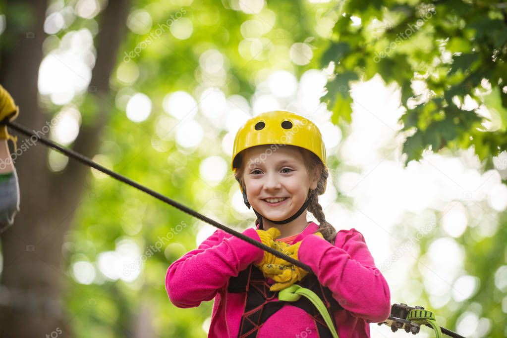 Happy little child climbing on a rope playground outdoor. Cute child in climbing safety equipment in a tree house or in a rope park climbs the rope. Toddler kindergarten.