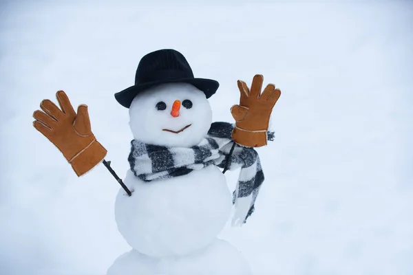 Kar taneleri ve kardan adamla kışın. Kardan adam kırmızı burunlu, kış şapkası ve eşarbıyla duruyor.. — Stok fotoğraf