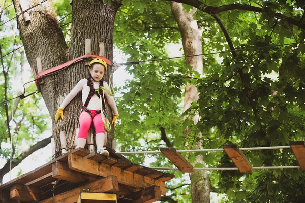 Girl climbing on a rope playground outdoor. Rope way - little girl is looking at the rope slideway fearing. Looking away with fear of extreme rope slide.