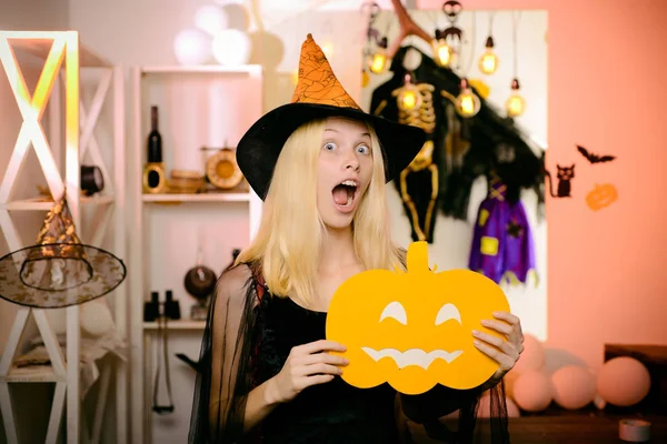 Surprised woman in witches hat and short dress. Vampire Halloween Woman portrait. Beautiful young surprised woman in witches hat and costume holding pumpkin. Funny face. Crazy people.