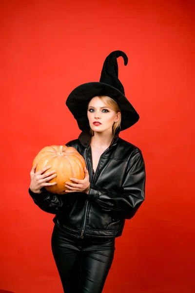 Jovens mulheres em trajes de bruxa negra halloween em festa sobre fundo vermelho. Bruxa posando com abóbora. — Fotografia de Stock
