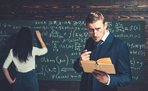 Strenger Lehrer mit Brille, der Erklärungen gibt, während er ein Buch in der Hand hält. Nachhilfelehrer hilft seiner jungen Schülerin in Mathe. privates Bildungskonzept — Stockfoto