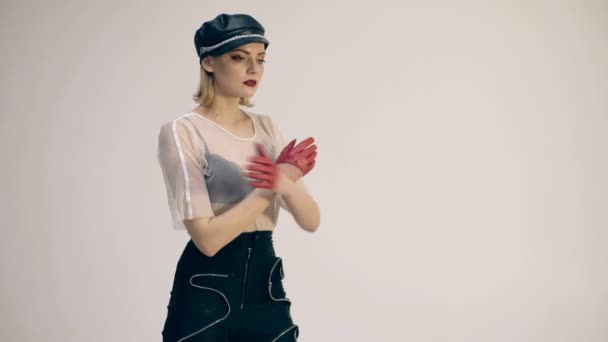 Belle femme en chapeau et gants en cuir. Fille mannequin. Femme dominante portant des vêtements militaires rouges et noirs en cuir, y compris des gants et un bonnet. Un cosplay fétiche. Fond blanc . — Video