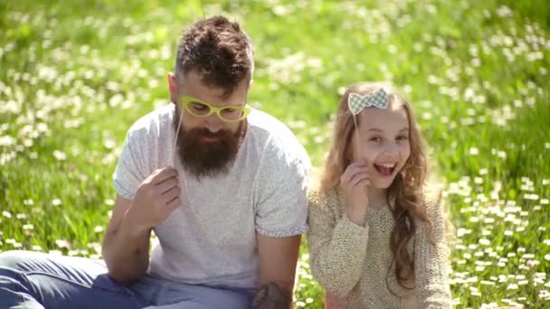 Best friends concept. Dad and daughter sits on grass at grassplot, green background. Family spend leisure outdoors. Child and father posing with glases, bow and tie. Family day concept. — Stock Video