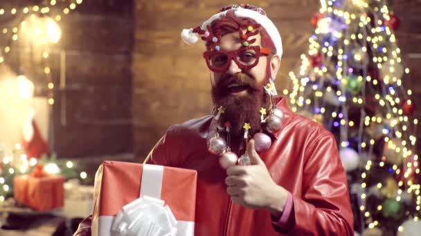 Новогоднее платье. Бородатый сумасшедший смотрит в камеру. Привлекательный бородатый хипстер. Рождественская елка Рождественский Санта желает счастливого Рождества. Хипстерский современный Санта-Клаус поздравляет с Рождеством . — стоковое видео