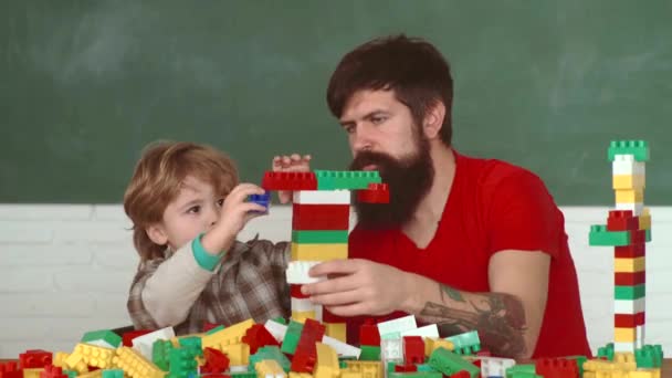 ワークショップで木製の板を穴あけドリルで父と小さな息子。子供の少年と父親は、自宅でビルダーを果たします。レンガや石のブロックから壁を構築する小さな息子のレンガ造り. — ストック動画