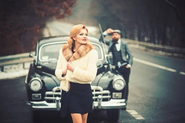 Coppia innamorata ad un appuntamento romantico. Retro raccolta auto e riparazione auto da parte del macchinista. Viaggi e viaggi d'affari o autostop. Accompagnamento della ragazza da parte della sicurezza. Uomo barbuto e donna sexy in pelliccia . — Foto Stock