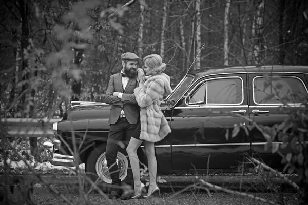 Casal apaixonado no encontro romântico. Retro coleta de carro e reparação de automóveis por motorista mecânico. Viagem e viagem de negócios ou engate caminhadas. Homem barbudo e mulher sexy em casaco de peles. Escolta de menina por segurança . — Fotografia de Stock