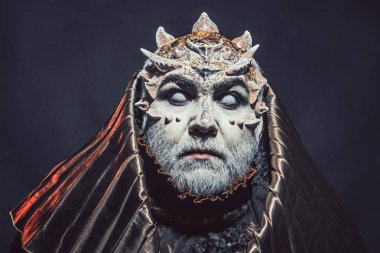 Beyaz sakallı komuta sizde canavar gibi giyinmiş. Adam dikenler veya siğiller ile yüz pırıltılar ile kaplı. Siyah zemin üzerine altın kukuleta ile iblis. Fantezi kavramı. Uzaylı, iblis, büyücü makyaj