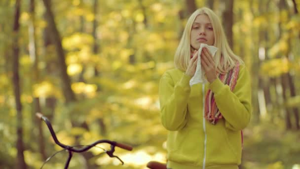 Una donna fa una cura per il comune raffreddore nel parco autunnale. Stagione influenzale fredda, naso che cola. Mostrando donna malata starnutire al parco autunnale . — Video Stock