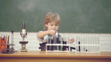 Arka planda tahta olan sınıf odasındaki çocuk. Laboratuvar mikroskobu ve test tüpleri. Evde eğitim. Kimya deneyimim. Junior yıl kimya.