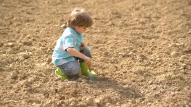 Erken çocukluk gelişimi. Bahar alanında spud ile çalışan sevimli küçük çiftçi - kırsal arka plan ile çiftlikte çocuk çiftçi ekim - çocuk çiftçi kavramı.