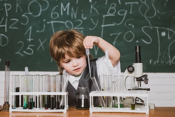 Il ragazzo sta imparando in classe sullo sfondo della lavagna. Scienze chimiche. Scienza. Bambino delle elementari. Esperimenti di biologia con microscopio . — Foto Stock