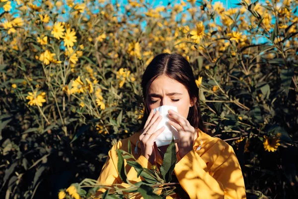 La mujer se está sonando la nariz cerca de las flores en flor. Jovencita estornudando y sosteniendo papel en una mano y ramo de flores en la otra. Gripe . — Foto de Stock