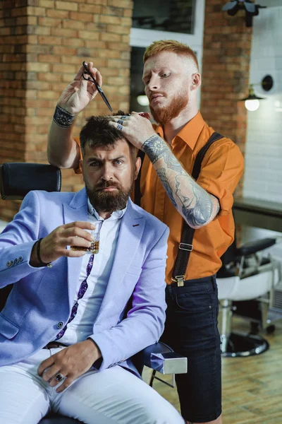 Ideias sobre barbearia e salão de barbeiro. Um brutamontes na Barbearia moderna. Cabeleireiro faz penteado um homem com barba. Barbeiro - raspas e aparas. Cuidados com a barba . — Fotografia de Stock