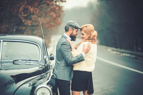 Homem barbudo e mulher sexy em casaco de peles. Viagem e viagem de negócios ou engate caminhadas. Retro coleta de carro e reparação de automóveis por motorista mecânico. Escolta de rapariga pela segurança. Casal apaixonado na data romântica — Fotografia de Stock