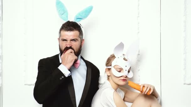 Brutal couple in leather masks eat fruits and vegetables. Concept of healthy food. Bearded man with bunnies ears eats an apple. Woman in leather mask eats a carrot. Brutal couple eating healthy food.