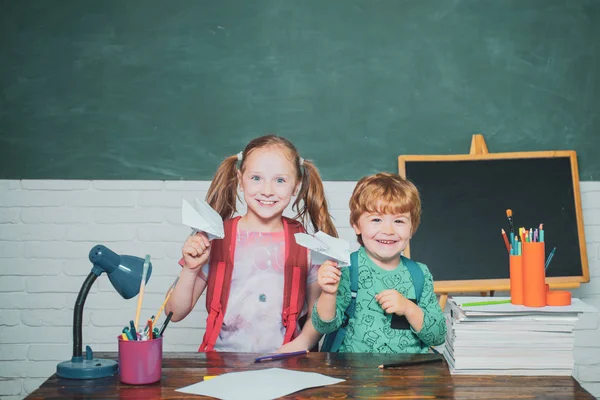Wróć do szkoły i szczęśliwego czasu. Śmieszne małe dziecko bawią się na tle tablicy. Przyjazne dziecko w klasie bawią się papierowym samolotem w pobliżu tablicy biurowej. — Zdjęcie stockowe