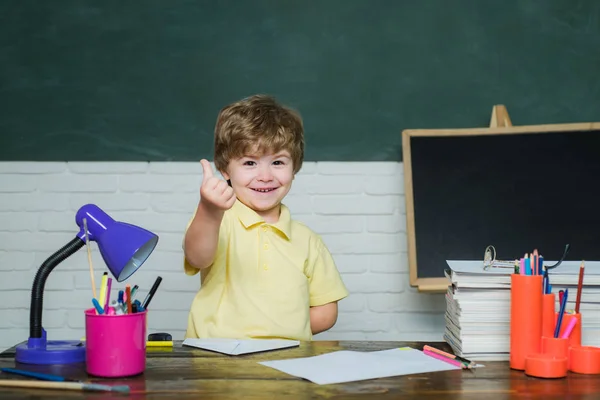 Kleine jongen leerling met Happy Face Expression in de buurt van Bureau met school supplies-school concept. Schattige kleine Preschool Kid Boy in een klaslokaal. — Stockfoto