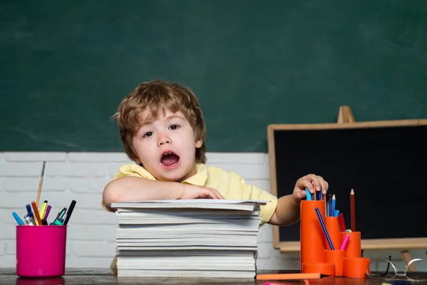 Happy cute clever boy pupil with book. Kid with a book. Funny little child having fun on blackboard background. Kids with a book. Boy Pupil from elementary school at the school yard. — Stock Photo, Image