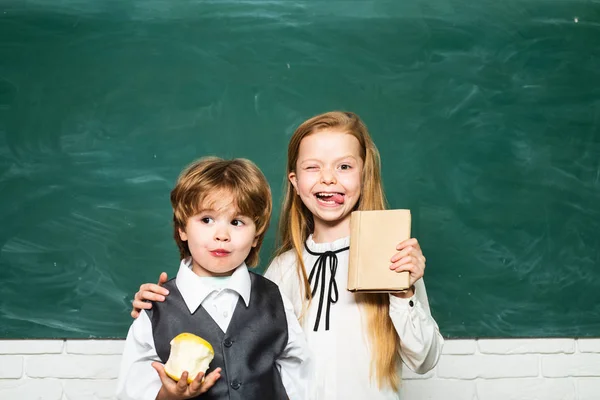 Fröhliche Stimmung, die in der Schule breit lächelt. Bildung. Kleine Kinder in der Schulstunde. Mädchen und Junge mit glücklichem Gesichtsausdruck neben Schreibtisch mit Schulsachen. Schulkonzept. — Stockfoto