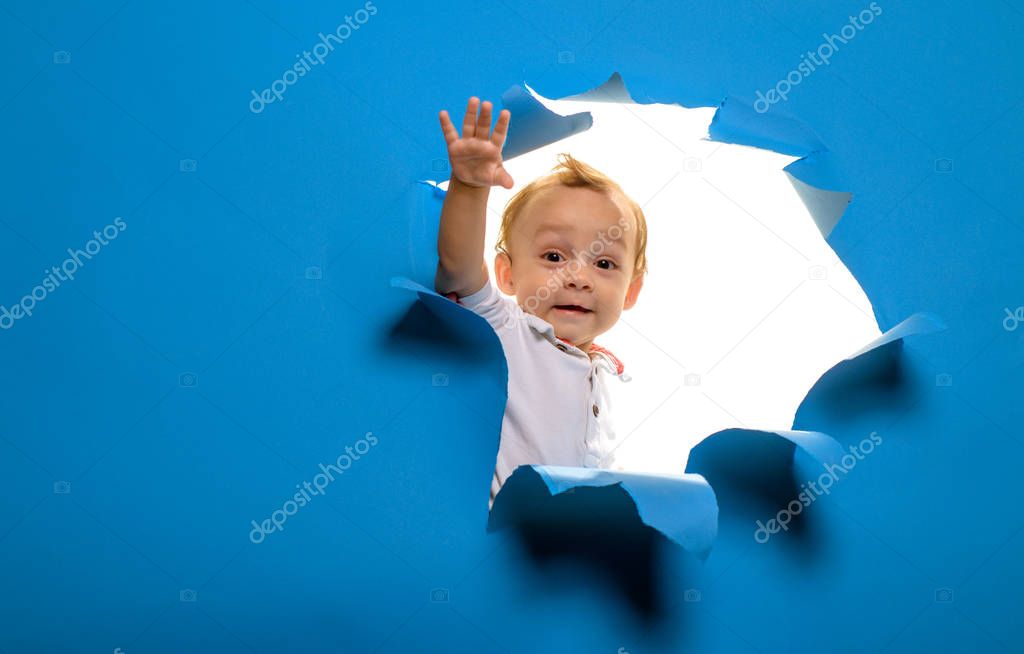 Hi there. Entrance to new life or beginning. Curious boy child look out of hole in paper. Little kid cutting through blue wall. Little child peek through torn paper. Being curious, copy space