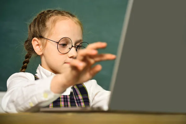 Μικρό μαθητή μαθητή με φορητό υπολογιστή. Πρώτη φορά στο σχολείο. Μικρή μαθήτρια με χαρούμενη έκφραση προσώπου κοντά στο γραφείο με σχολικά εφόδια. Κοντινό. — Φωτογραφία Αρχείου