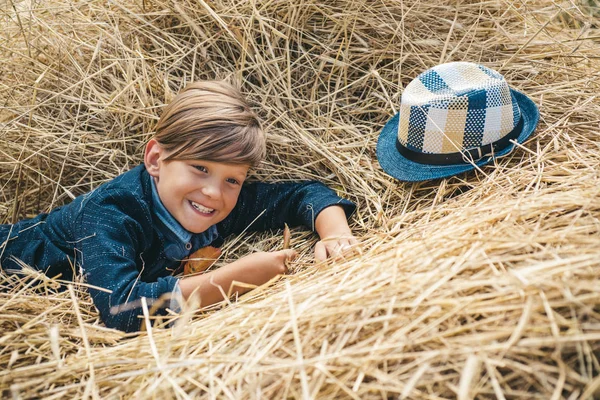 Lille pojke annonserar naturliga produkter. Pojken annonserar barnkläder till hösten. Porträtt av en glad pojke som ligger i ett hö. Happy Child på höst mässan. — Stockfoto