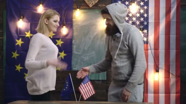 Hipsters mulher e homem apertando as mãos sobre bandeiras americanas e da UE. Aperto de mão sobre bandeiras americanas e da UE. Cooperação entre EUA e União Europeia. Conceito de amizade dos povos. Bandeira no fundo . — Vídeo de Stock