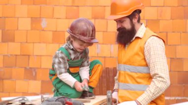 Baba ve Oğul Birlikte Ev İnşa Ediyor. Çocukluk kavramı. Turuncu kask veya kask lı küçük çocuk sakallı babasına yardım eder. Çocuk çocuk ve baba evde inşaatçılar oynamak.