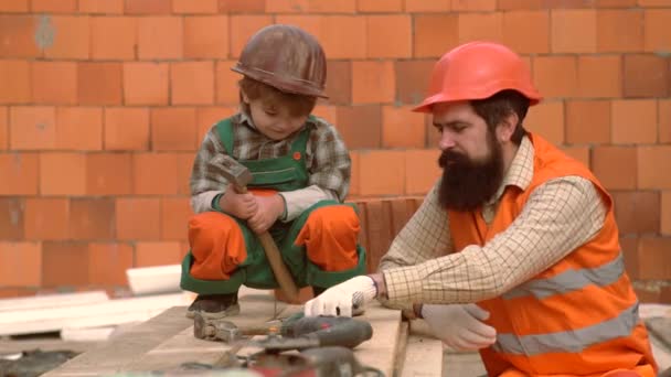 Sohn und Vater legen einen Ziegelstein, um eine Mauer zu bauen. Arbeit mit Werkzeugen. Der kleine Sohn hilft seinem Vater beim Bauen. Jungen spielen als Bauarbeiter oder Reparateur. glückliche Familie baut ein Haus. — Stockvideo