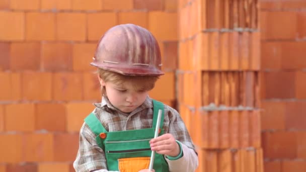 Conceito de infância. Um rapazinho a sonhar com um novo lar. Filho ajudante. Criança e obras. Bonito menino edifício casa . — Vídeo de Stock