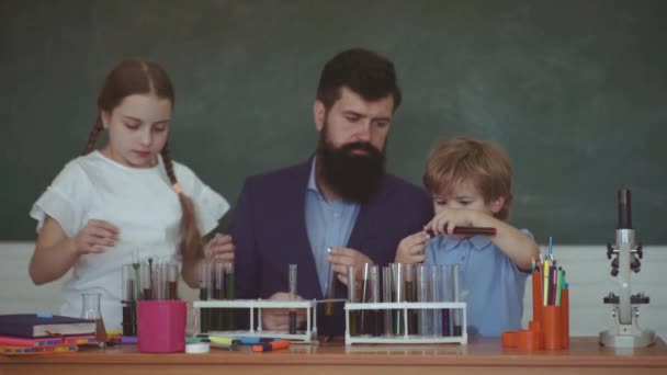 Děti a učitel se učí ve třídě na pozadí tabule. Zpátky do školy. Veselý usměvavý žák na stole. — Stock video