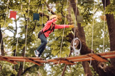 Toddler anaokulu. Küçük çocuk çocukluk yılları zevk. Mutlu küçük çocuk bir ağaca tırmanıyor. Ağaçlar arasında bir halat parkında güzel bir çocuğun portresi. Kask-çocuk oynama için güvenlik donanımları.