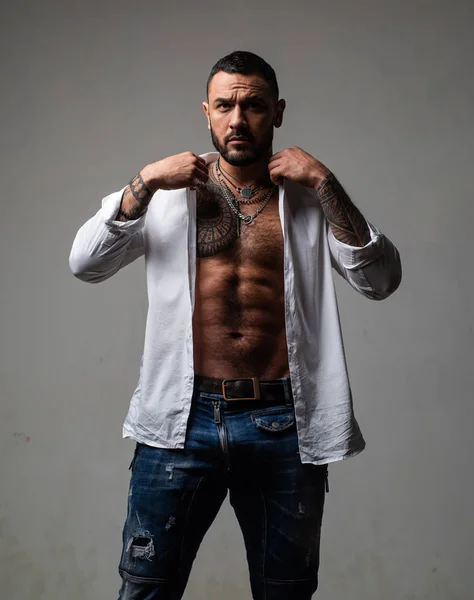 Genç sakallı adamın moda portresi. Gri üzerinde izole kamera bakıyor. Yakışıklı bir maço. Dövme ile Brutal sakallı koç.