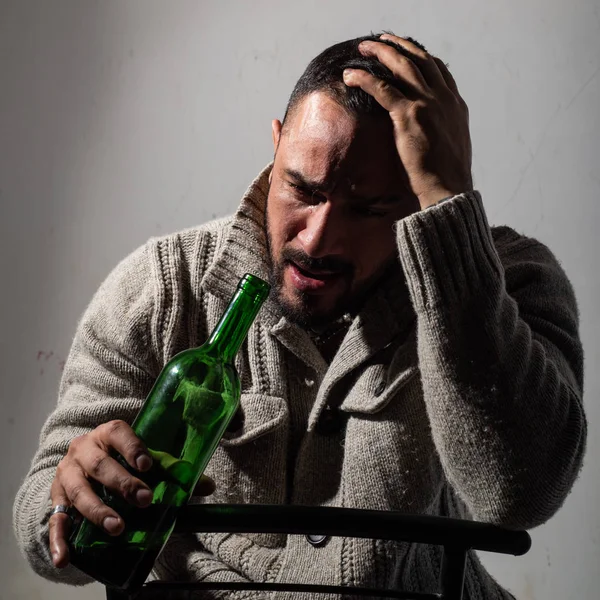Alcoholism, alcohol addiction and people concept. Frustrated man with bristle is holding his head, crying and sitting with a bottle in his hands. Depression. Disorders of health. — Stock Photo, Image