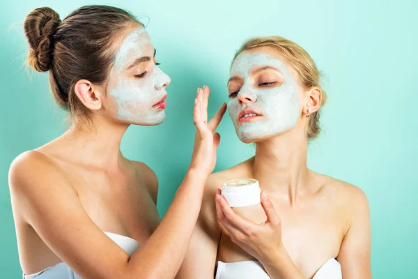 Two young women applying moisturizer cream on their face. Photo of careful friends receiving spa treatments. Home grooming. — Stock Photo, Image