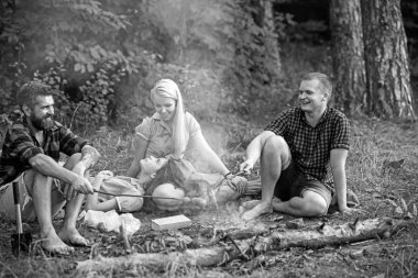 Kamp ateşinde sosisleri kızartan kampçılar, kızartma çubuklarında sosis kavuruyorlar. Arkadaşları veya turistler ile Yangın yeri alev yakınında oturuyor