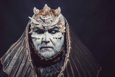 Adam dikenler veya siğiller ile yüz pırıltılar ile kaplı. Siyah zemin üzerine altın kukuleta ile iblis. Beyaz sakallı komuta sizde canavar gibi giyinmiş. Fantezi kavramı. Uzaylı, iblis, büyücü makyaj