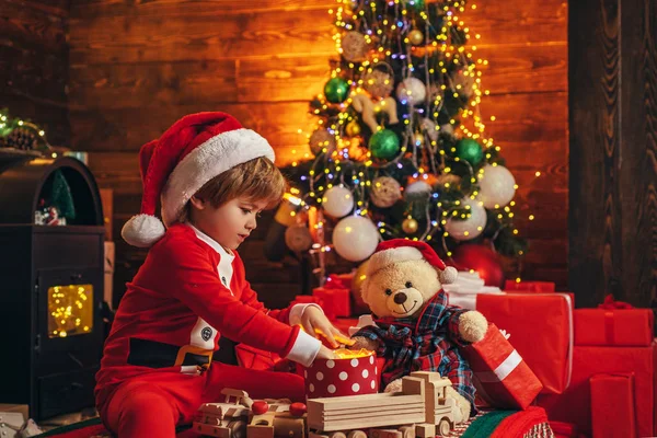 Christmas Kids Story Konzept. Erste Erinnerung an die Kindheit. Weihnachtswunder und Neujahrsgefühle. Ein kleiner Junge in warmer Kleidung sitzt und spielt mit Holzspielzeug Geschenk. Spiele mit offenem Ausgang. — Stockfoto