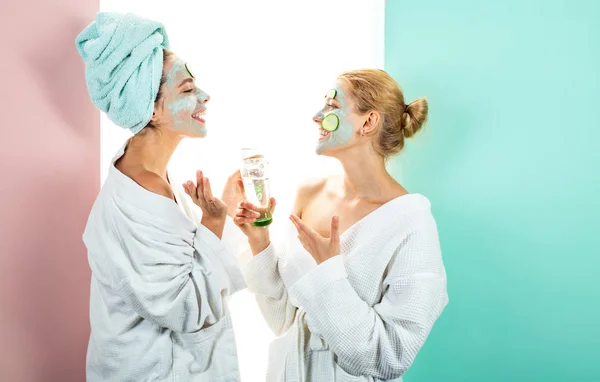 Próprio salão de spa em casa. Concepção de cuidados com a pele usando máscara branca e pepinos no rosto. Duas irmãs têm fim de semana . — Fotografia de Stock