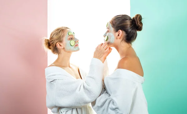 Twee vrouwelijke zussen hebben weekend in de slaapkamer. Conceptie van de huidverzorging door het gebruik van verse komkommer ringen en wit masker op het gezicht. — Stockfoto