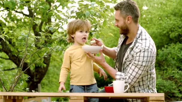 Bébé enfant gai mange de la nourriture elle-même avec une cuillère. Heureux père avec son fils jouant au parc d'automne. Un petit garçon affamé qui mange. Père et enfant . — Video