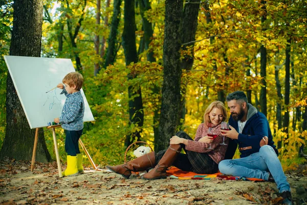 Painting skills. Mom and dad relax park picnic while kid painting. Rest and hobby concept. Parents watching their little son painting picture in nature. Art and self expression. Talent development