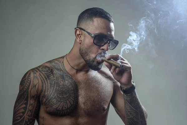 muscular macho man with athletic body. sexy abs of tattoo man. sport and fitness, health. confidence charisma. brutal sportsman torso. steroids. smoking cigarette. exhale smoke. bad habit. harmful