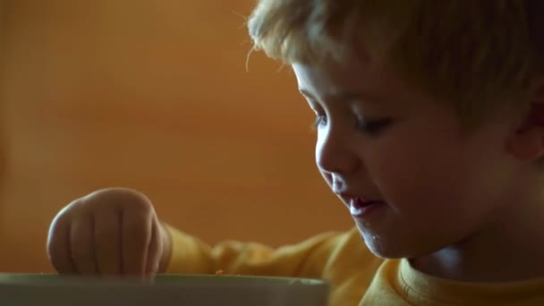 Anak muda duduk di meja makan makanan sehat dengan ekspresi lucu di wajah. Anak itu makan. Anak manis sedang makan. Anak kecil sedang sarapan di dapur. Makanan dan minuman untuk anak-anak . — Stok Video