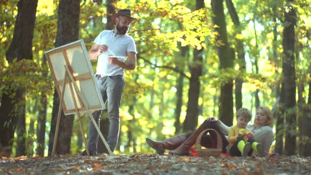 Ehemann Künstler Zeichnung Bild auf Herbst Natur. buntes Herbst-Familienporträt. glückliches junges Paar mit männlichen Kindern im Freien. — Stockvideo